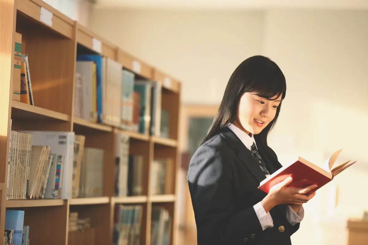 女子高生が図書館で立ちながら本を読んでいる画像