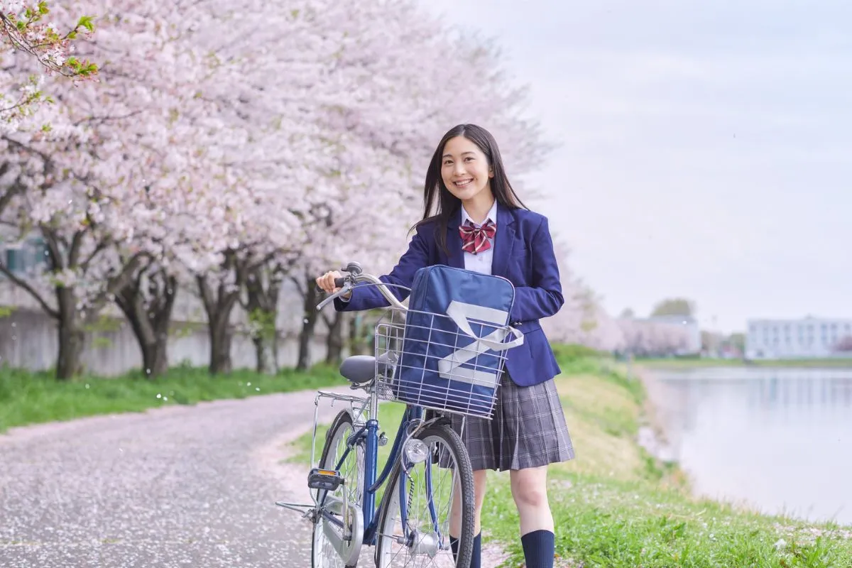 女子高生が桜並木を自転車を押して進む画像